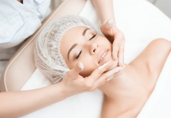 The doctor is doing a face massage for the girl. The doctor applies a special cream to the skin. The girl came to the procedure of laser hair removal. They are in the modern beauty salon.